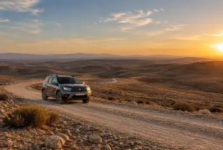 Voiture tout-terrain sur une piste caillouteuse du désert d’Agafay, collines arides au coucher du soleil