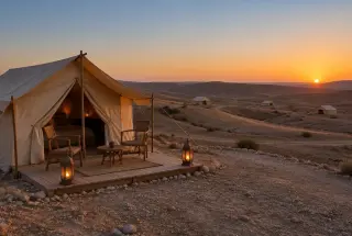 Tente beige éclairée par des lanternes au coucher du soleil dans le désert pierreux d’Agafay.